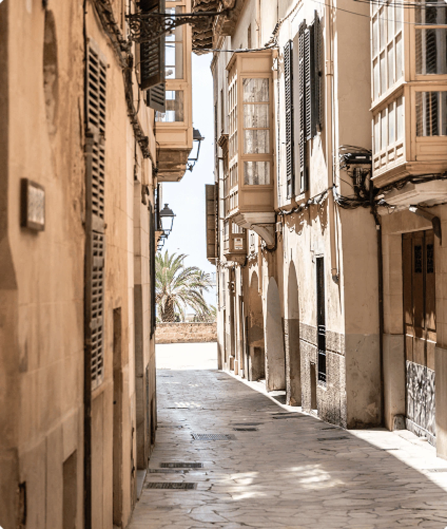 Sunlit narrow street in Palma Old Town featuring historic architecture and enclosed balconies